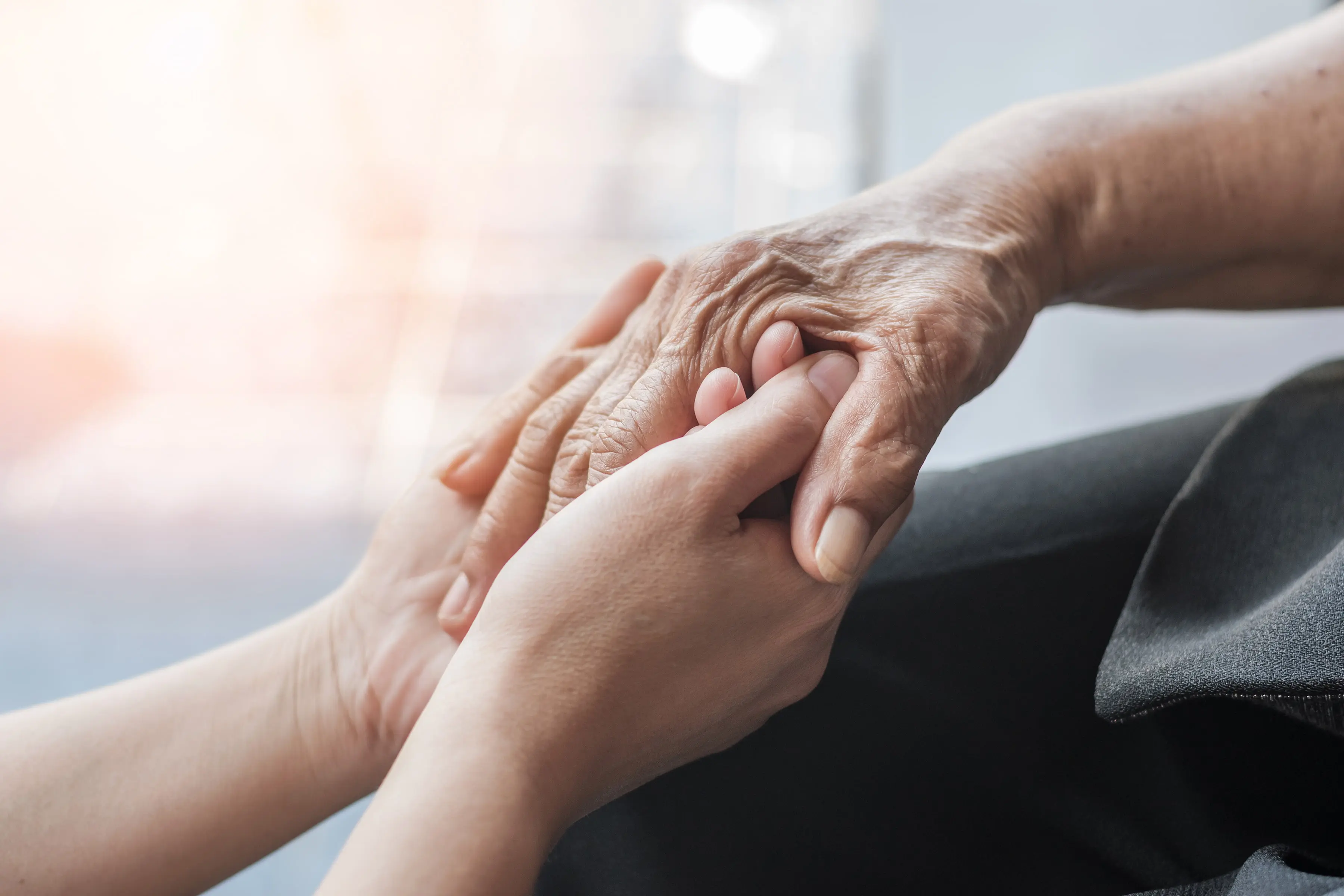 Eine betreuende Person hält einfühlsam die Hand eines älteren Menschen