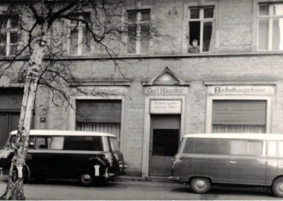 Historische Außenaufnahme des Bestattungshauses Schade in Guben mit zwei Bestattungsfahrzeugen vor dem Gebäude.