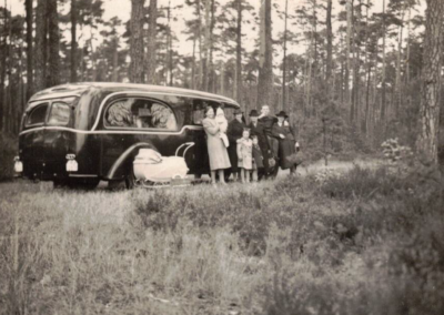 Historische Aufnahme eines Bestattungsfahrzeugs der Familie Schade mit Personen in einem Waldgebiet bei Guben.